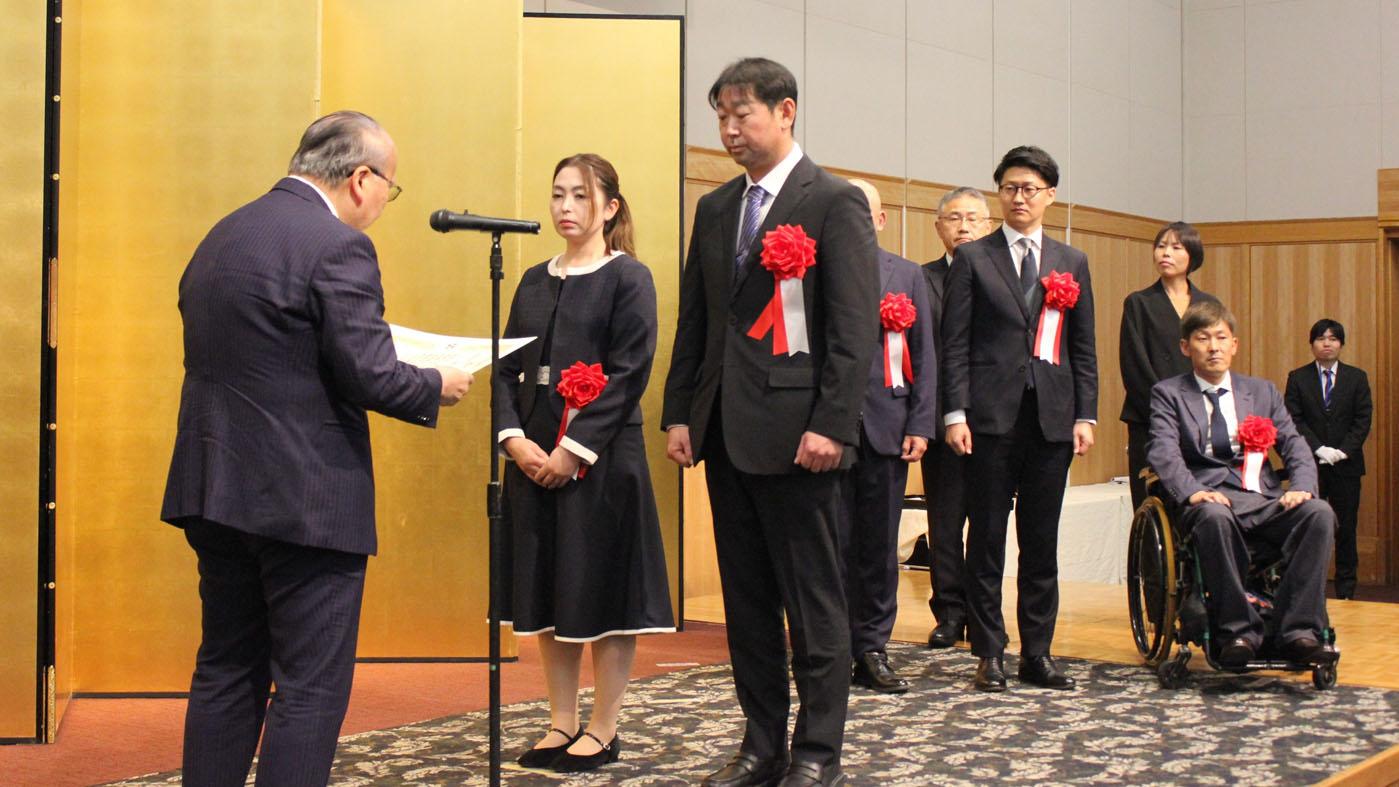壇上で表彰される藤田貴良さん、麻奈美さん夫妻